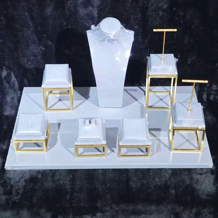 Gold display stands with white cushions and a tall central podium on a white platform