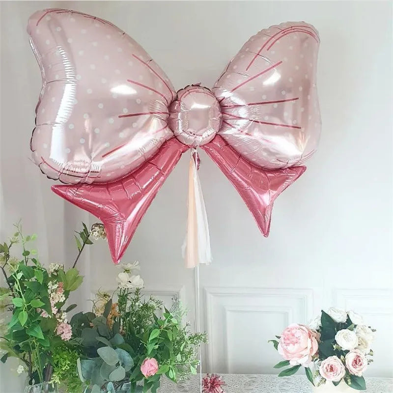 Pink bow-shaped foil balloon with polka dots above flower arrangements